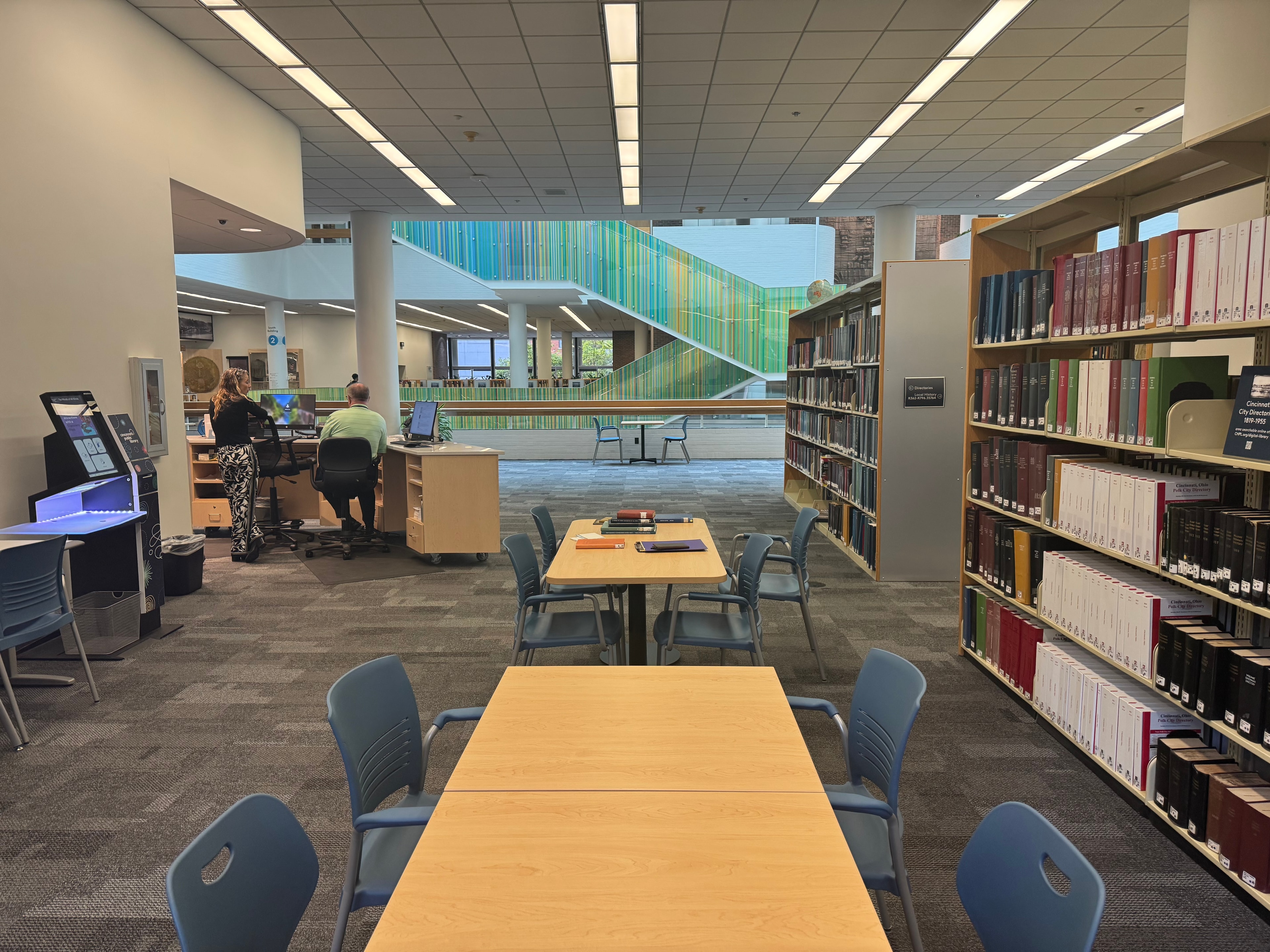 Cincinnati Public Library reading room with research tables, computers, collection shelving, and colorful staircase